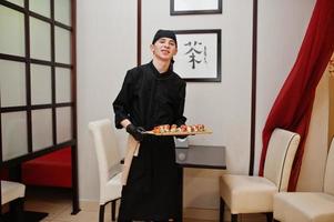 professionele chef-kokslijtage in het zwart met sushi en broodjes in een restaurant met traditionele japanse gerechten. foto