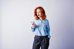 portret van een jonge roodharige zakenvrouw in blauw shirt en broek sms'en aan de telefoon. foto