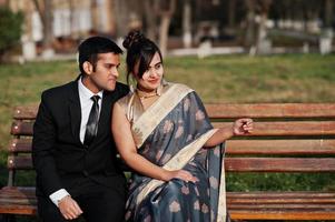 elegante en modieuze Indiase vrienden paar vrouw in saree en man in pak zittend op de bank. foto
