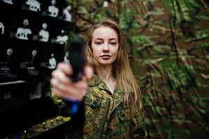 militair meisje in camouflage uniform met pistool bij de hand tegen leger achtergrond op schietbaan. foto