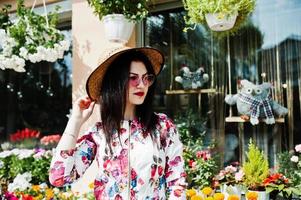 zomer portret van brunette meisje in roze bril en hoed tegen bloemenwinkel. foto