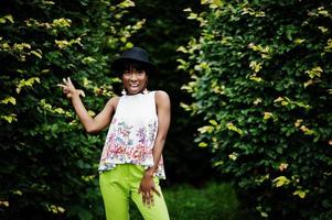 geweldige Afro-Amerikaanse modelvrouw in groene broek en zwarte hoed poseerde met verschillende emoties in het park, toont een twee vingers. foto