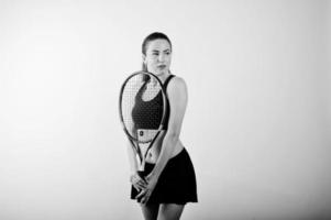 zwart-wit portret van een mooie jonge vrouw in sportkleding die een tennisracket vasthoudt terwijl hij tegen een witte achtergrond staat. foto