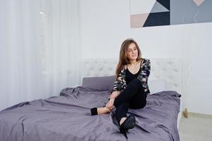 knappe brunette meisje draagt militair shirt, poseren op bed in de studio. studiomodel portret. foto