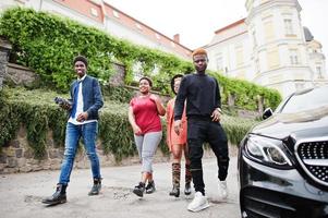 vier afrikaanse vrienden lopen in de buurt van luxe auto buitenshuis. twee zwarte meisjes met jongens. foto