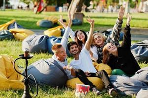 jonge multi-etnische groep mensen kijken naar film op poef in openluchtbioscoop. foto