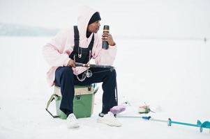 Afro-Amerikaanse visser met hengel en thermoskan. winter vissen. foto