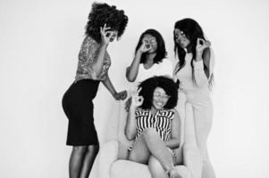 gelukkige heldere positieve momenten van vier Afrikaanse meisjes. plezier hebben en lachend op stoel tegen witte lege muur. mooie momenten van vier beste vrienden. ok teken tonen. foto
