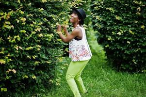 geweldige Afro-Amerikaanse model vrouw in groene broek en zwarte hoed gesteld in het park. foto