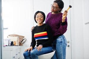 Afro-Amerikaanse vrouw die make-up toepast door visagist bij beauty salon. foto