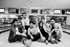 groep van vijf Zuid-Aziatische volkeren die rust en plezier hebben in de bowlingclub, zittend op een bowlingbaan met ballen op handen. foto
