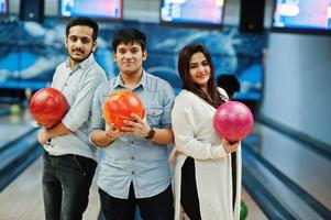 drie Zuid-Aziatische vrienden in jeans shirt bij bowlingclub met ballen op handen. foto