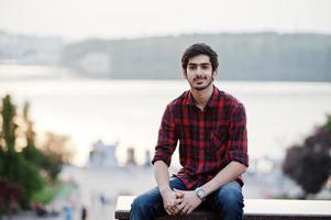 jonge Indiase student man op rood geruit hemd en jeans poseerde in de stad. foto