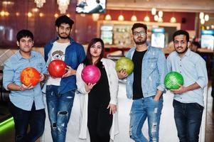 groep van vijf Zuid-Aziatische volkeren die rust en plezier hebben in de bowlingclub met ballen bij de hand. foto