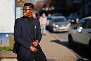 verbazingwekkend uitziende Afro-Amerikaanse man draagt een blauwe blazer met broche, zwarte coltrui en een bril op straat. modieuze zwarte man. foto