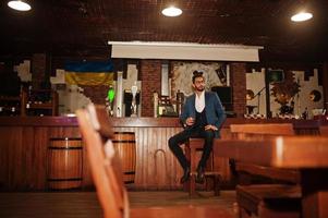 knappe goed geklede arabische man met glas whisky en sigaar poseerde in de pub. foto