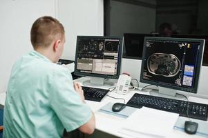 medisch thema. arts in het mri-kantoor in het diagnostisch centrum in het ziekenhuis, zittend in de buurt van monitoren van een computer met menselijk brein erop. foto