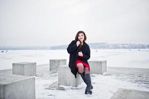 brunette plus size model op rood tegen bevroren meer op winterdag. foto