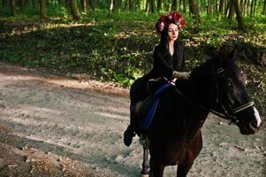 mystieke meisje in krans slijtage in het zwart bij paard in hout. foto