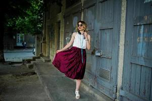modieuze en mooie blonde model meisje in stijlvolle rood fluwelen velours rok, witte blouse en zonnebril, gesteld met telefoon en koptelefoon. foto