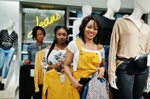 drie Afrikaanse vrouw poseerde in de buurt van mannequins in kledingwinkel. winkeldag bij jeanssector. foto