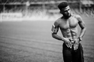 Afro-Amerikaanse mannelijke atleet sexy sport blote torso man met lopende sport arm case voor mobiele telefoon, gesteld op groen gras van voetbalstadion. foto