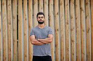 knappe lange Arabische baard man model op gestript shirt buiten tegen houten achtergrond gesteld. modieuze Arabische man. foto