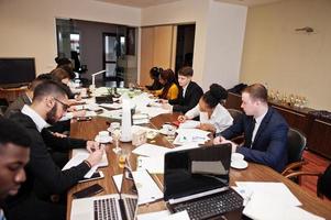 multiraciaal businessteam spreekt vergadering rond bestuurstafel toe, werkt samen en schrijft iets op papier. foto