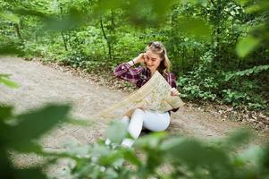 portret van een positieve jonge prachtige blonde zittend op de grond met een kaart in haar handen in het bos. foto
