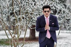 elegante Indiase macho man model op pak en roze stropdas, zonnebril geposeerd op winterdag toont namaste. foto