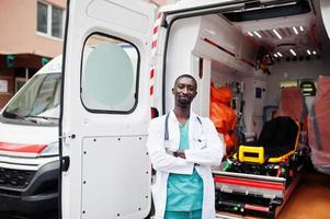 Afrikaanse mannelijke paramedicus die zich voor ziekenwagenauto bevindt. foto