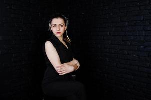 portret van een mooie brunette meisje in zwarte jumpsuit zitten en poseren in de studio. foto