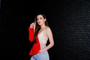 stijlvolle brunette meisje op rode jas tegen studio zwarte bakstenen muur. foto