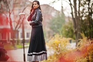 vrij indisch meisje in zwarte saree-jurk en leren jas poseerde buiten in de herfststraat. foto
