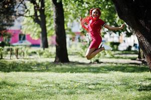 schattig en slank Afrikaans Amerikaans meisje in rode jurk met dreadlocks springen buiten in het voorjaarspark. stijlvol zwart model. foto