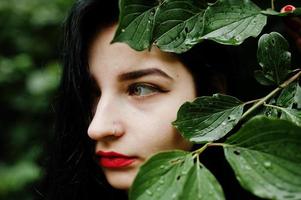 close-up portret van sensuele brunette meisje met rode lippen. goth dramatische vrouw bij boomtak. foto