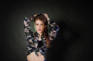 knappe brunette meisje draagt militair shirt en spijkerbroek, poseren in studio tegen een grijze achtergrond. studiomodel portret. foto