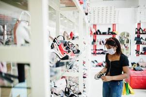 afro-amerikaanse vrouw die gezichtsbeschermend medisch masker draagt voor bescherming tegen virusziekte in schoenenwinkel tijdens coronaviruspandemie. foto