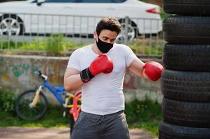 portret sport arabische bokser man in zwart medisch gezichtsmasker boksen buiten tijdens coronavirus quarantaine. foto