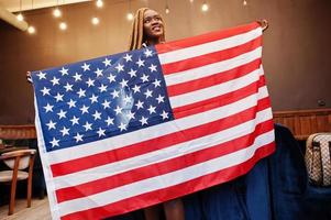 mooie Afrikaanse vrouw in stijlvolle casual kleding poseren met usa vlag in handen in kantoor. foto