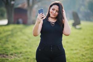 mooie latino model meisje uit ecuador slijtage op zwart gesteld op straat met mobiele telefoon. foto