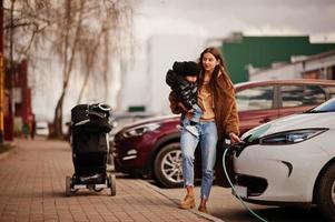 jonge moeder met kind elektrische auto opladen bij het elektrische tankstation. foto