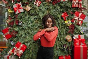 portret van een Afrikaanse vrouw met krullend haar, gekleed in modieuze rode coltrui die zich voordeed tegen kerstversiering, oudejaarsavondthema. foto