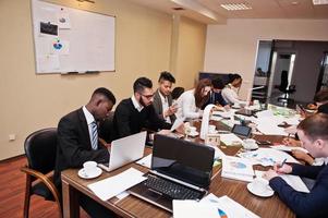 multiraciaal businessteam spreekt vergadering rond bestuurstafel toe, werkt samen en schrijft iets op papier. foto
