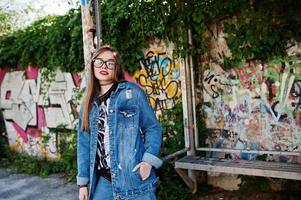 stijlvolle casual hipster meisje in jeans slijtage en bril tegen grote graffiti muur. foto