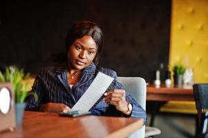 Afro-Amerikaanse zakenvrouw zittend aan tafel in café en heeft een cheque. zwarte meid die rust heeft. foto