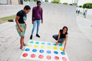 groep van drie Afro-Amerikaanse vrienden spelen twister-spel buiten. foto