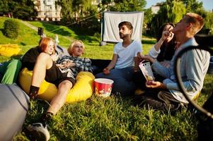 jonge multi-etnische groep mensen kijken naar film op poef in openluchtbioscoop. foto