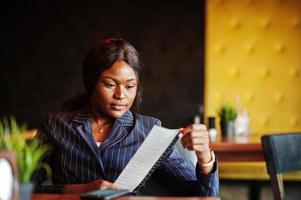 Afro-Amerikaanse zakenvrouw zittend aan tafel in café en heeft een cheque. zwarte meid die rust heeft. foto