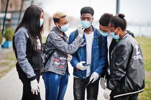 groep afrikaanse tieners vrienden in het park met medische maskers beschermen tegen infecties en ziekten coronavirus virus quarantaine, lees geschokt nieuws op de telefoon. foto